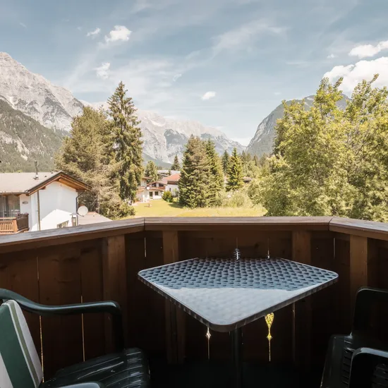 Mountain balcony with table and chairs overlooking alpine valley and pine trees